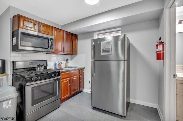 kitchen featuring brown cabinets, a sink, backsplash, stainless steel appliances, and baseboards