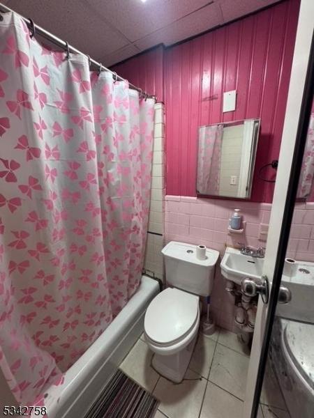 bathroom featuring shower / tub combo with curtain, tile walls, a paneled ceiling, toilet, and tile patterned floors