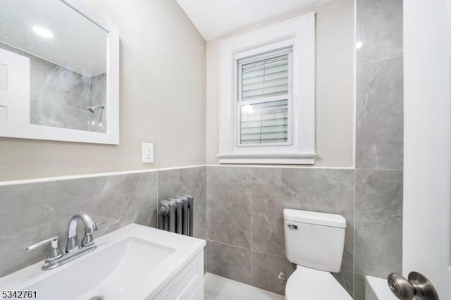 bathroom with radiator heating unit, vanity, toilet, and tile walls