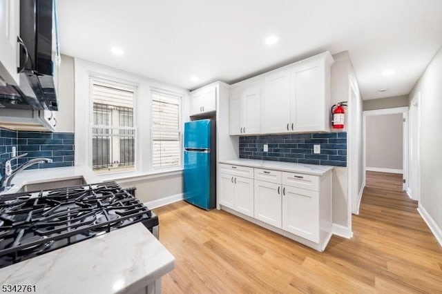 kitchen with light wood-style floors, freestanding refrigerator, white cabinetry, a sink, and baseboards