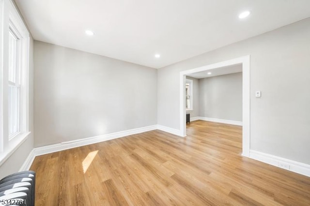 spare room with baseboards, light wood-style floors, recessed lighting, and radiator