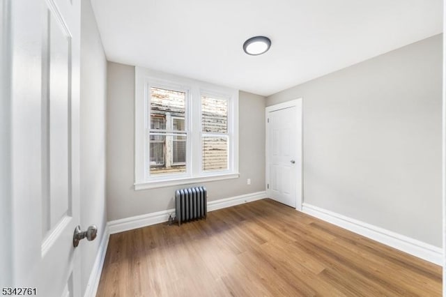 empty room with baseboards, radiator heating unit, and wood finished floors