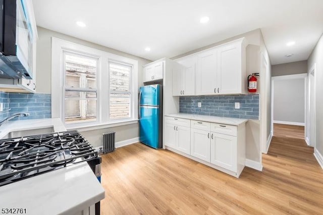 kitchen with light wood finished floors, white microwave, freestanding refrigerator, and white cabinets