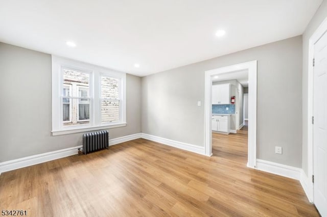 spare room featuring baseboards, light wood-type flooring, and radiator