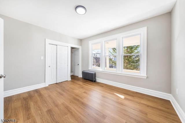 unfurnished bedroom featuring baseboards, light wood-type flooring, and radiator