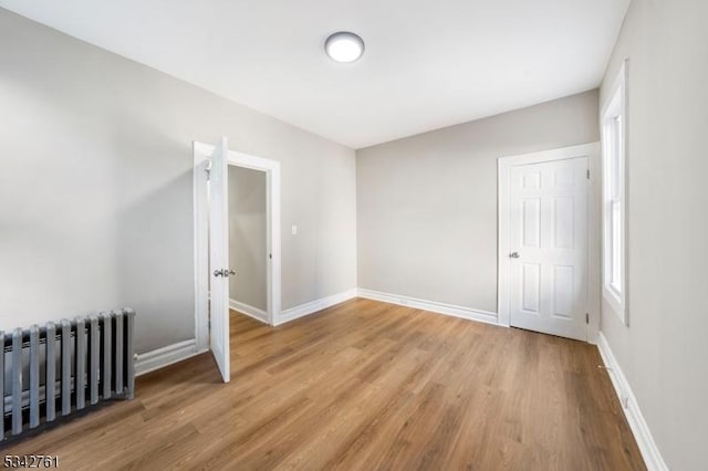 spare room with radiator, baseboards, and wood finished floors