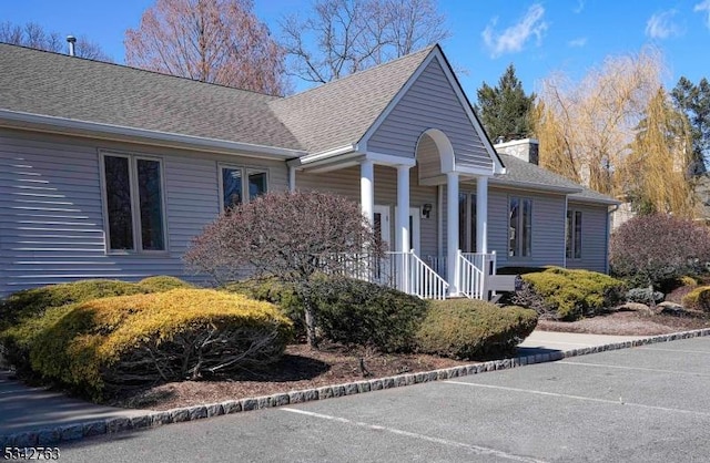 view of side of home featuring a shingled roof, covered porch, and a chimney