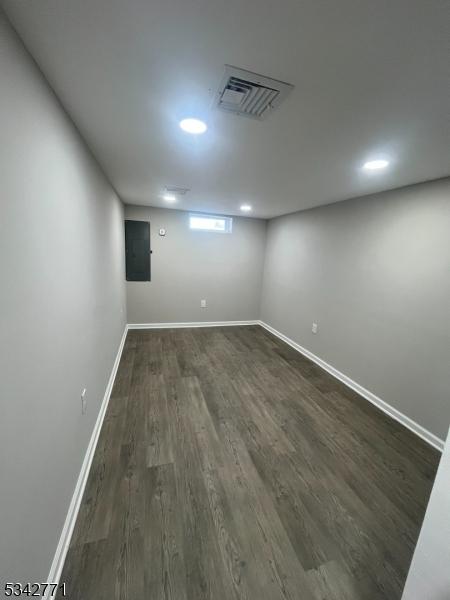 basement featuring dark wood-style flooring, visible vents, electric panel, and baseboards