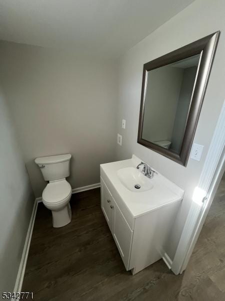 half bathroom with baseboards, vanity, toilet, and wood finished floors