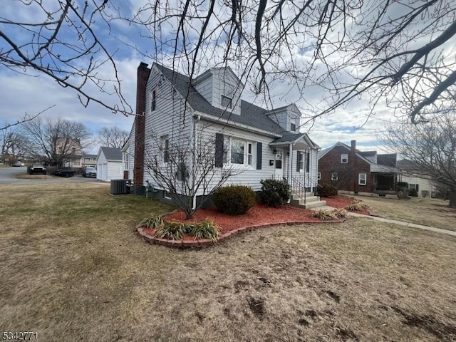 view of front facade featuring roof with shingles, a chimney, a front lawn, and central AC unit