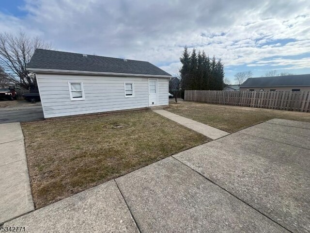 view of property exterior with a yard, fence, and a shingled roof