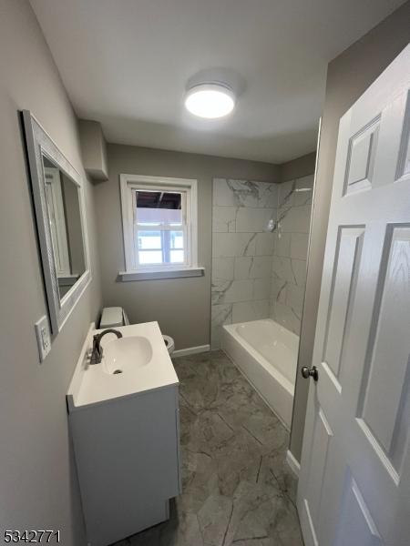 bathroom with baseboards, toilet, marble finish floor, vanity, and washtub / shower combination