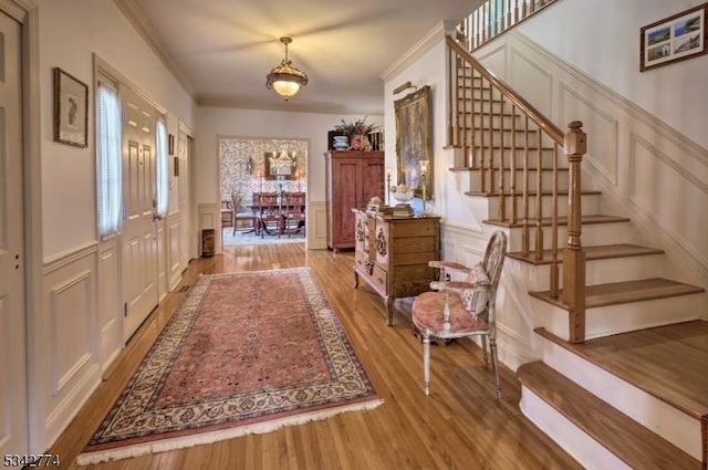 entrance foyer with stairway, light wood-type flooring, a decorative wall, and ornamental molding