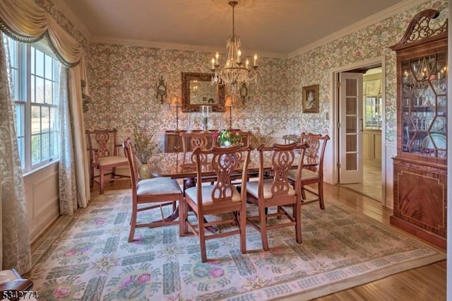 dining space featuring wallpapered walls, an inviting chandelier, wood finished floors, and ornamental molding