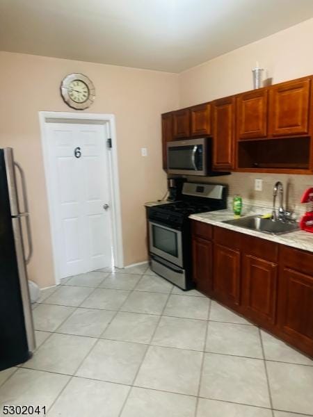 kitchen featuring light tile patterned floors, a sink, stainless steel appliances, light countertops, and backsplash