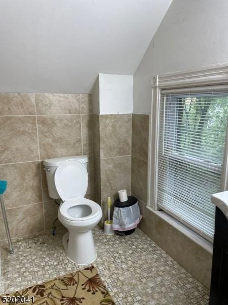 bathroom featuring lofted ceiling, tile patterned flooring, toilet, vanity, and tile walls