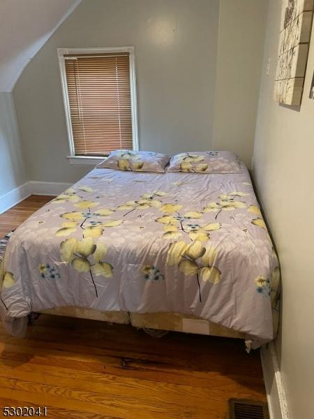 bedroom with visible vents, vaulted ceiling, baseboards, and wood finished floors