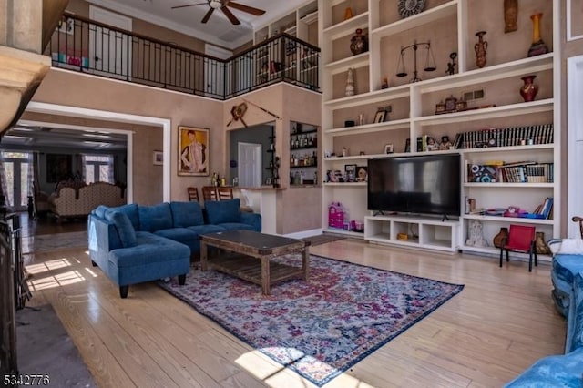 living room with ceiling fan, a high ceiling, wood finished floors, and built in features