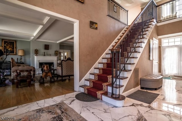 stairway with marble finish floor, a fireplace, crown molding, a high ceiling, and baseboards