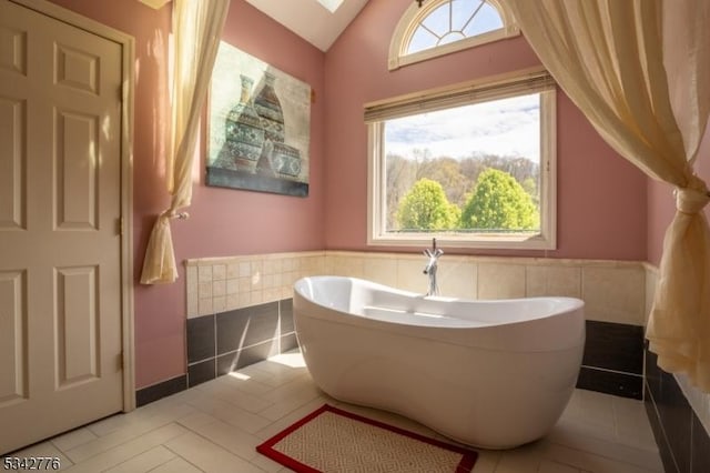 full bath featuring lofted ceiling with skylight, wainscoting, a freestanding tub, and tile walls