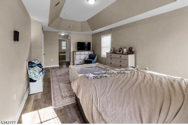 bedroom with a tray ceiling, visible vents, baseboards, and wood finished floors