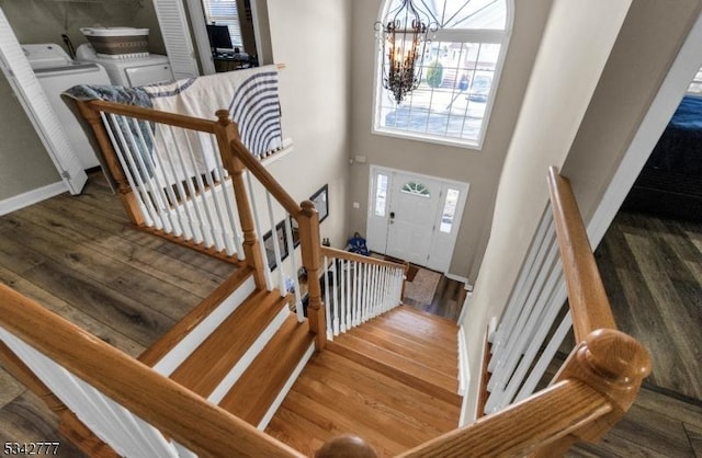 foyer entrance with a towering ceiling, a notable chandelier, washing machine and dryer, and wood finished floors