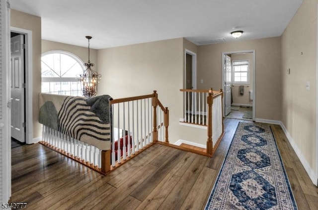 corridor with a chandelier, wood finished floors, an upstairs landing, and baseboards