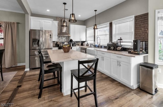 kitchen featuring backsplash, white cabinets, a kitchen island, wood finished floors, and stainless steel fridge