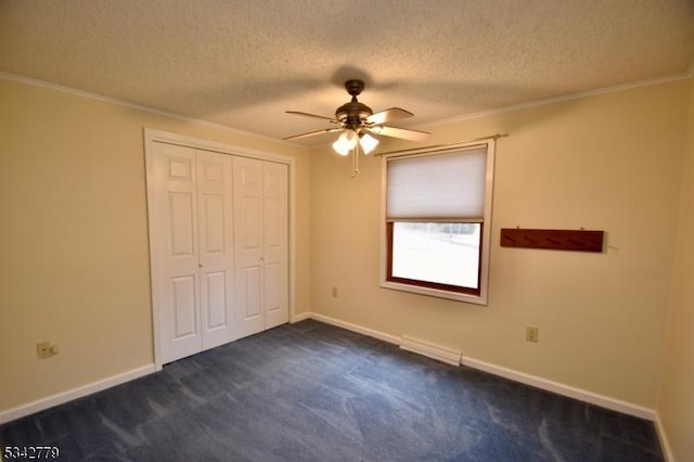 unfurnished bedroom featuring baseboards, a closet, a textured ceiling, crown molding, and dark colored carpet