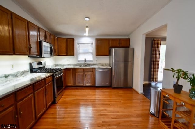 kitchen featuring brown cabinetry, light wood-style flooring, stainless steel appliances, and a sink