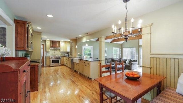kitchen with wall chimney range hood, appliances with stainless steel finishes, a peninsula, light wood-style flooring, and dark countertops