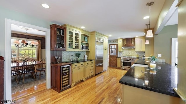 kitchen featuring high quality appliances, wall chimney range hood, beverage cooler, light wood-style floors, and recessed lighting