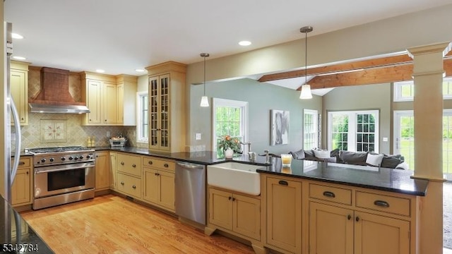 kitchen featuring stainless steel appliances, wall chimney exhaust hood, a sink, dark countertops, and light wood-type flooring