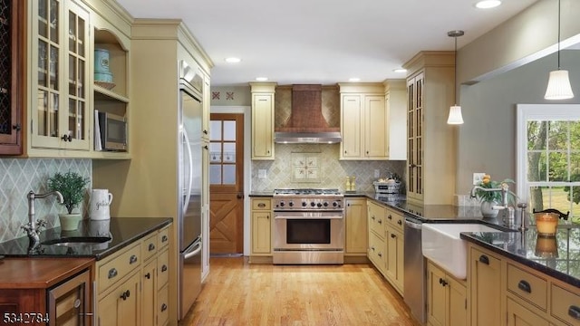 kitchen featuring high end appliances, custom range hood, cream cabinetry, a sink, and recessed lighting
