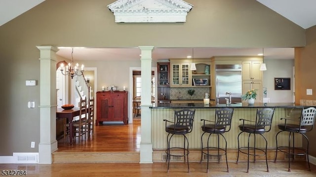 kitchen with built in fridge, ornate columns, a kitchen bar, light wood-type flooring, and high vaulted ceiling