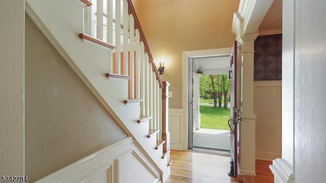 foyer entrance featuring light wood-style floors, stairway, a wainscoted wall, a towering ceiling, and decorative columns