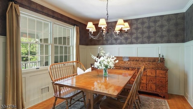dining area featuring a chandelier, light wood finished floors, a wainscoted wall, ornamental molding, and a decorative wall