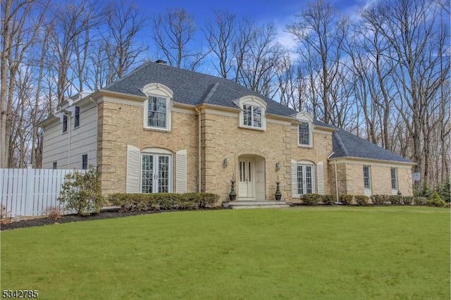 french provincial home with a front yard, fence, brick siding, and roof with shingles