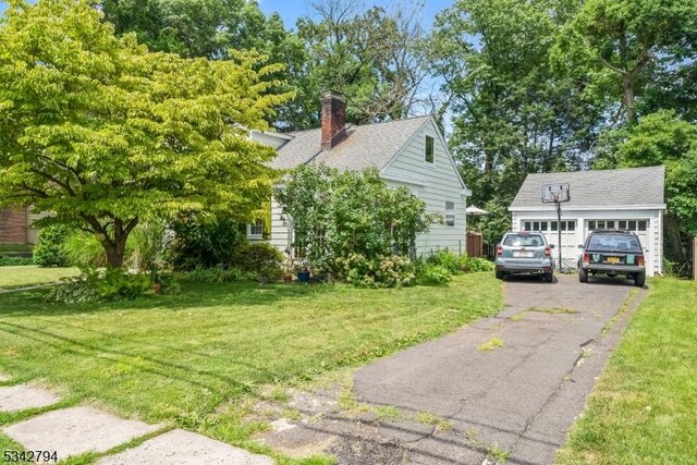 view of home's exterior featuring aphalt driveway, an outdoor structure, roof with shingles, a lawn, and a chimney