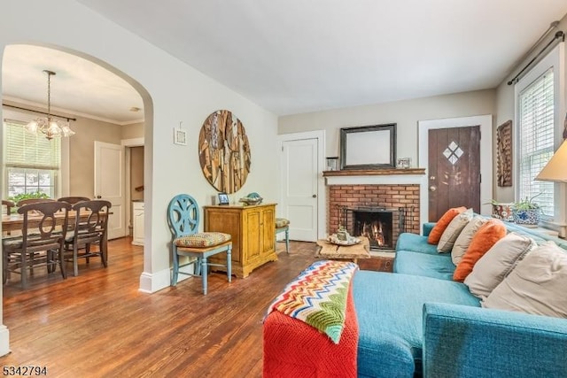 living room with arched walkways, a fireplace, baseboards, dark wood finished floors, and an inviting chandelier