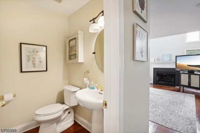 bathroom with a fireplace with flush hearth, toilet, baseboards, and wood finished floors