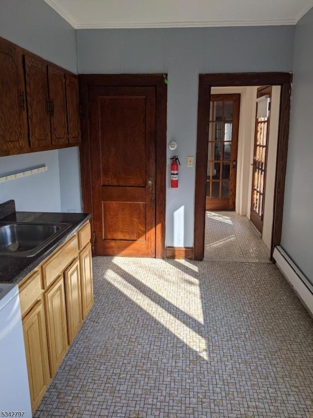 kitchen with dark countertops, baseboard heating, crown molding, and a sink