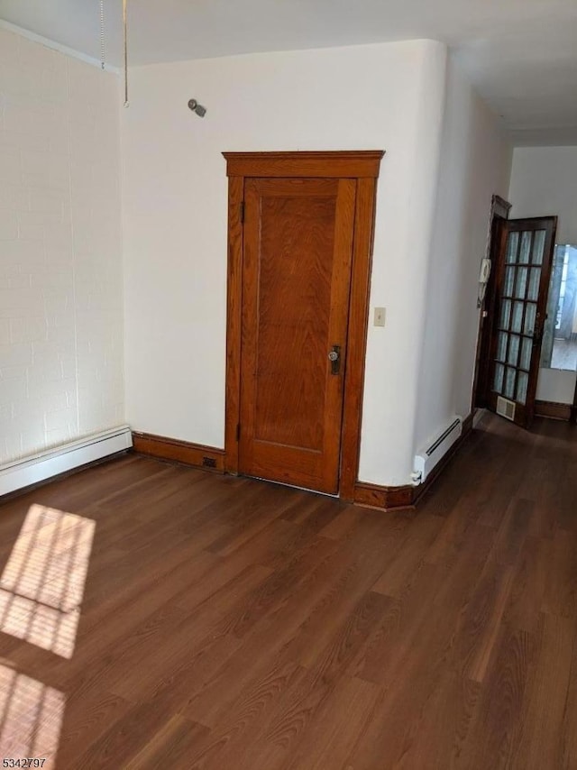 empty room featuring a baseboard heating unit, baseboards, and dark wood-style flooring