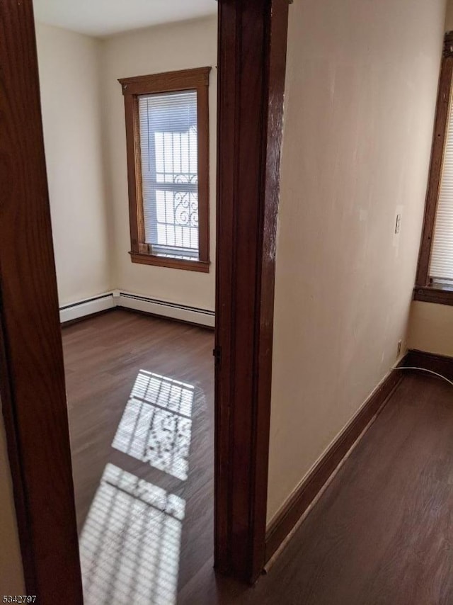 interior space with a baseboard heating unit, baseboards, and dark wood-style flooring