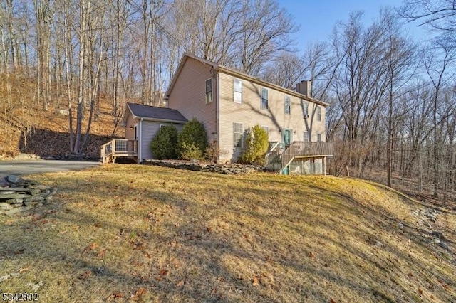 view of side of home featuring a chimney, a deck, and a yard