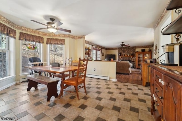 dining space with baseboards, ceiling fan, a stone fireplace, and baseboard heating