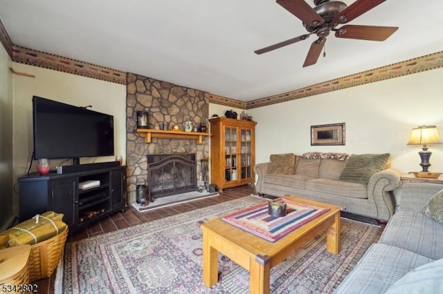 living area featuring a ceiling fan, a stone fireplace, and wood finished floors