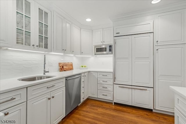 kitchen with built in appliances, white cabinetry, light countertops, and a sink