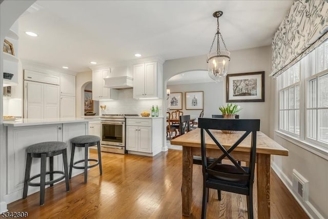 kitchen featuring custom exhaust hood, white cabinets, arched walkways, and high end stainless steel range