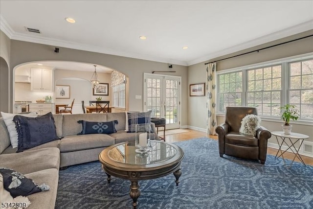 living room featuring visible vents, arched walkways, baseboards, and crown molding